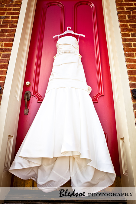 "Wedding dress hanging on red church door"